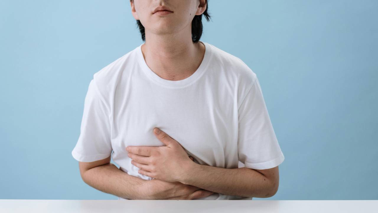 Person in a white t-shirt holding their stomach against a pale blue background