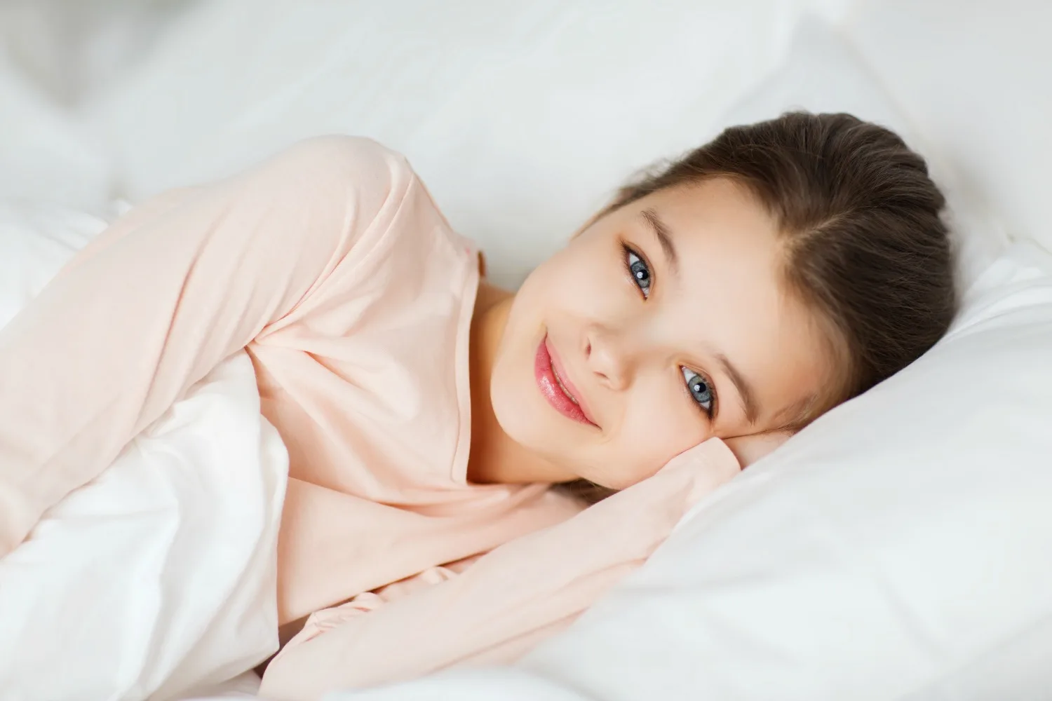 Girl in a peach top lying on white bedding and smiling