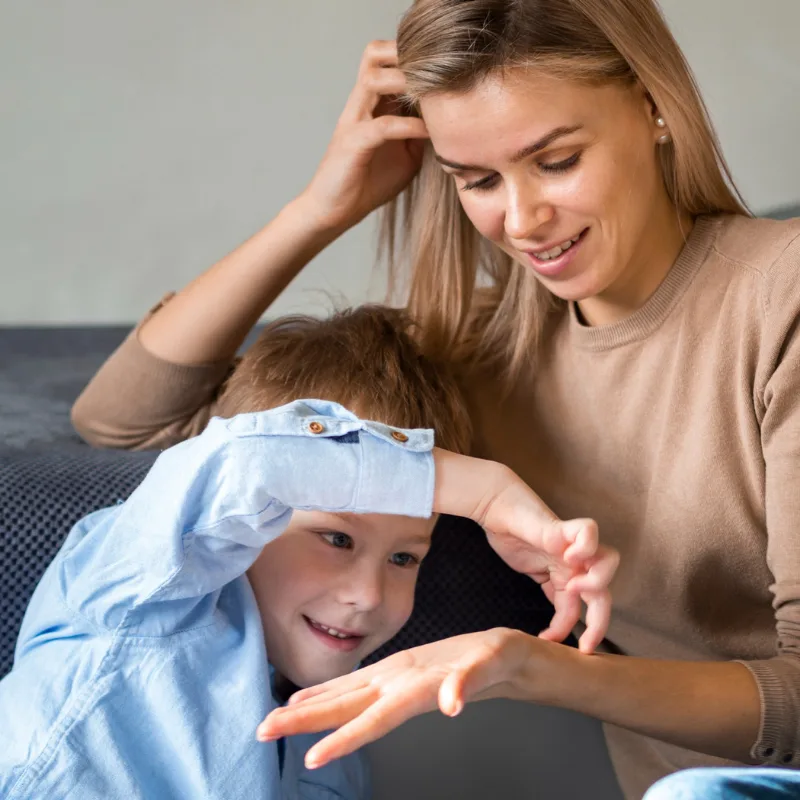Woman with a hand in her hair looking down at a boy in a light blue shirt who raises his hand to his head