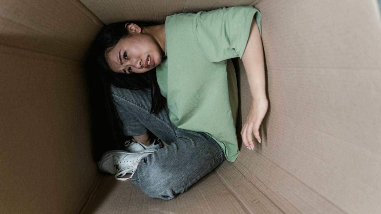 Person curled up inside a cardboard box on the floor