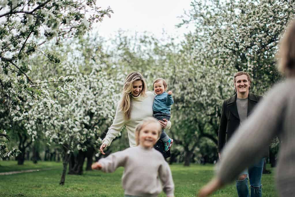 Happy family enjoying time together outdoors in a blooming orchard, with parents and children smiling and playing.
