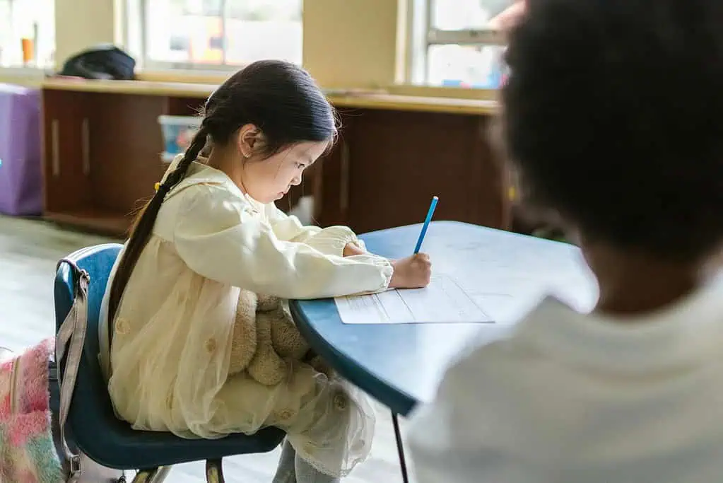 Young girl concentrating on her homework at a classroom desk, practicing focus as part of an ADHD friendly homework routine.