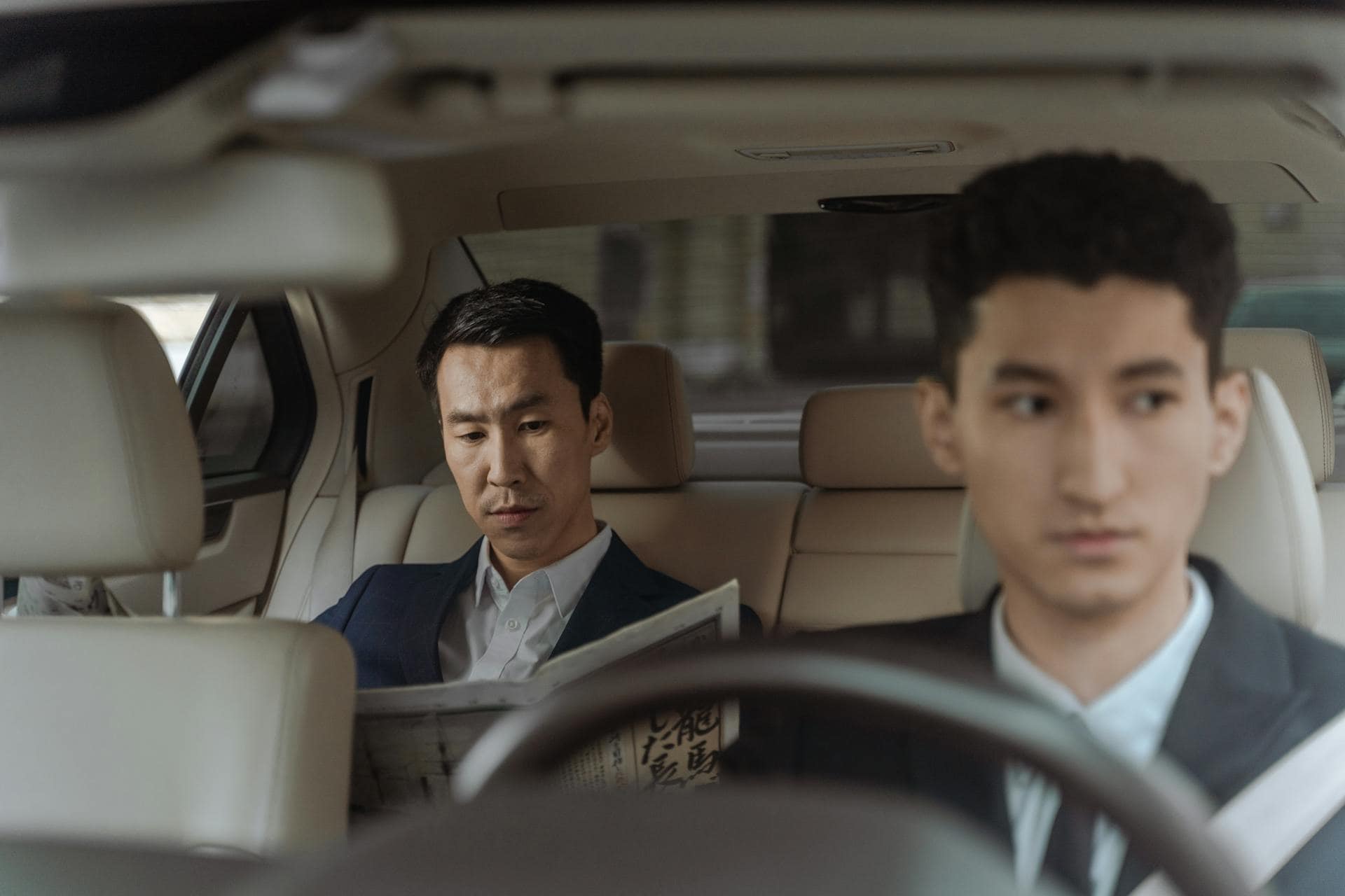 Two adult males in a car, one reading a newspaper in the back seat and the other appearing unfocused while driving capturing a moment that reflects distraction and mental drift often experienced in ADHD in adult males.