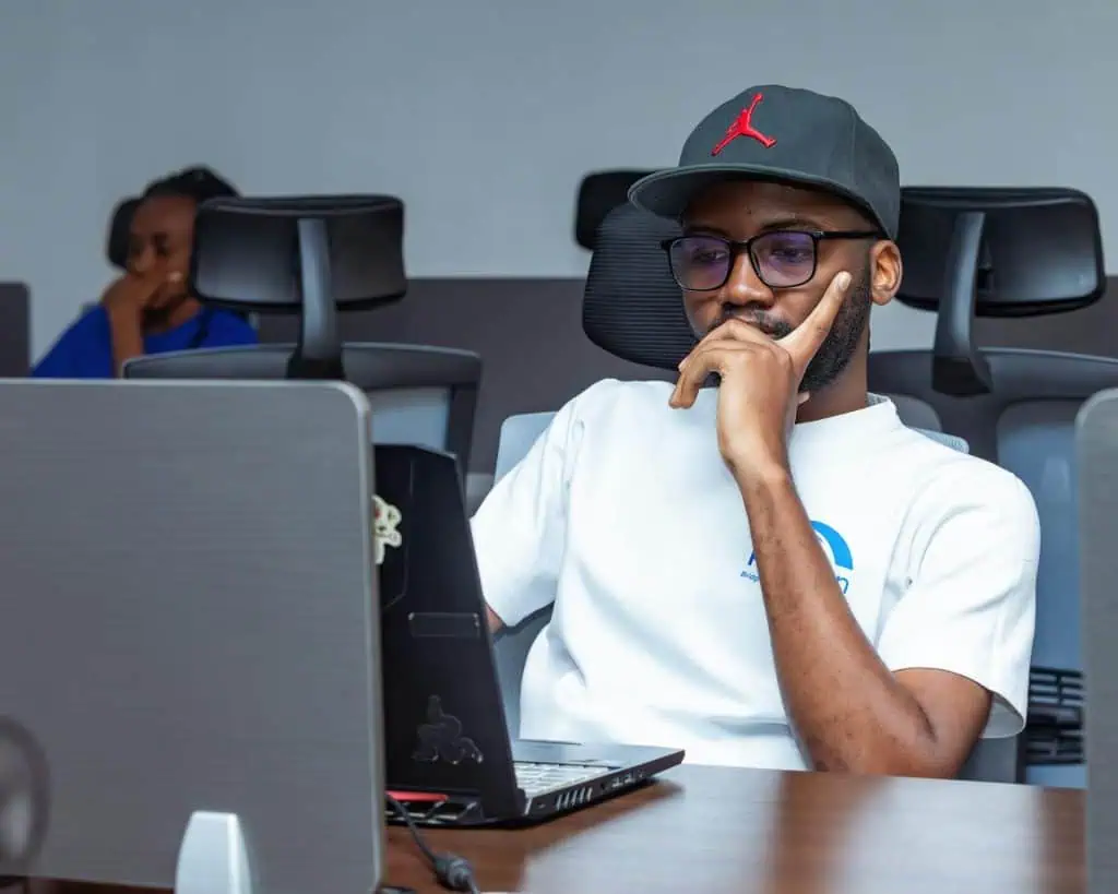 Adult male wearing a cap and glasses, seated in an office, looking deep in thought while using a laptop—illustrating focus challenges common in ADHD in adult males.