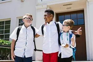 Three school children in uniforms with backpacks smiling and walking together after school. ADHD kids after school meltdown.