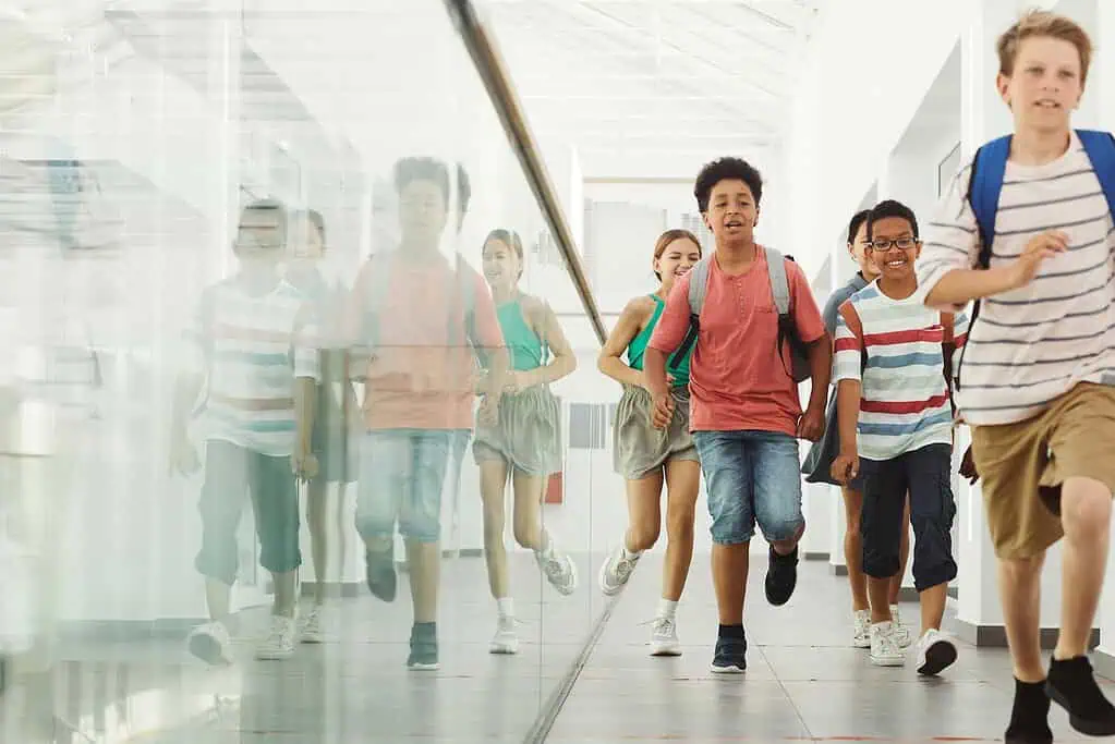 Group of school children with backpacks running and smiling after class in a hallway