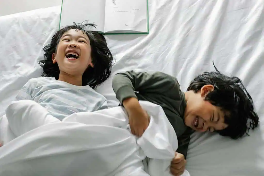 Two kids laughing and playing on a bed in the morning, showing a positive and joyful start to the day for children with ADHD.