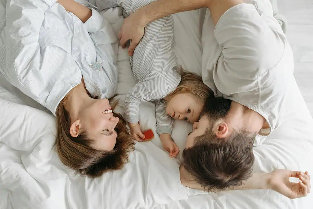 Mother, father, and young child lying together in bed, sharing a calm and intimate morning moment—demonstrating the importance of family connection in ADHD routines.