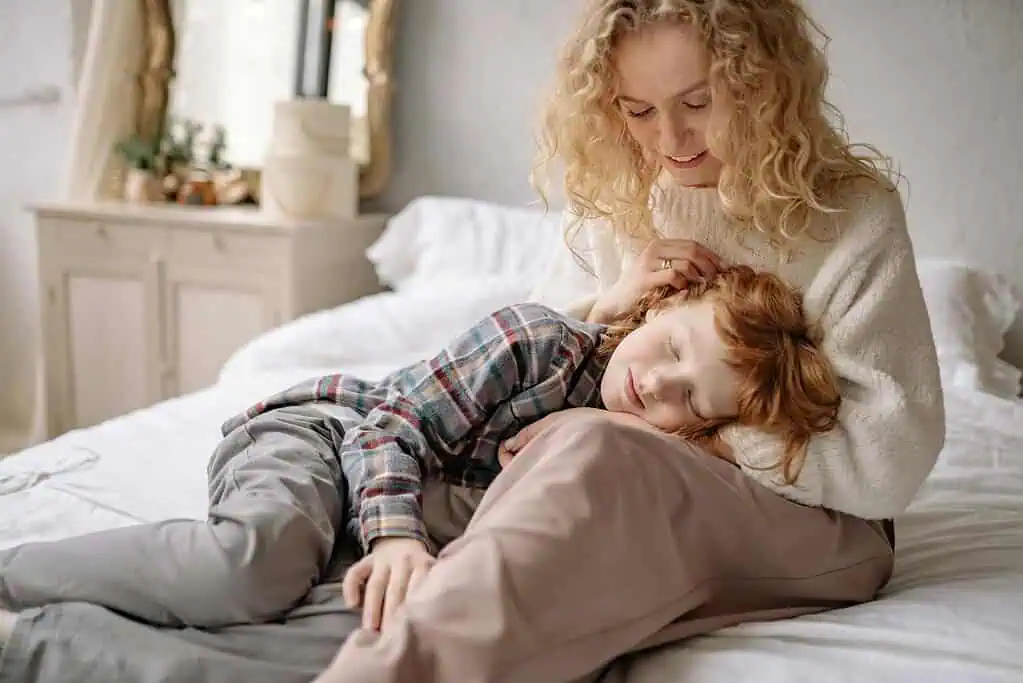 Mother comforting her child on the bed as the child peacefully rests on her lap, showing emotional support during sleep difficulties