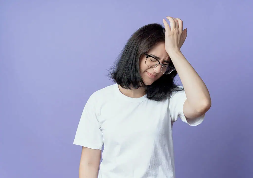 Young woman in glasses looking frustrated, touching her head—representing forgetfulness and daily struggles often experienced by women with ADHD.