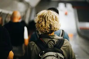 Back view of an adult with curly blonde hair wearing a backpack while walking through a busy station, symbolizing the daily challenges of dyspraxia in adults.