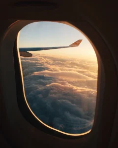 View of airplane wing and clouds through a window during sunset.