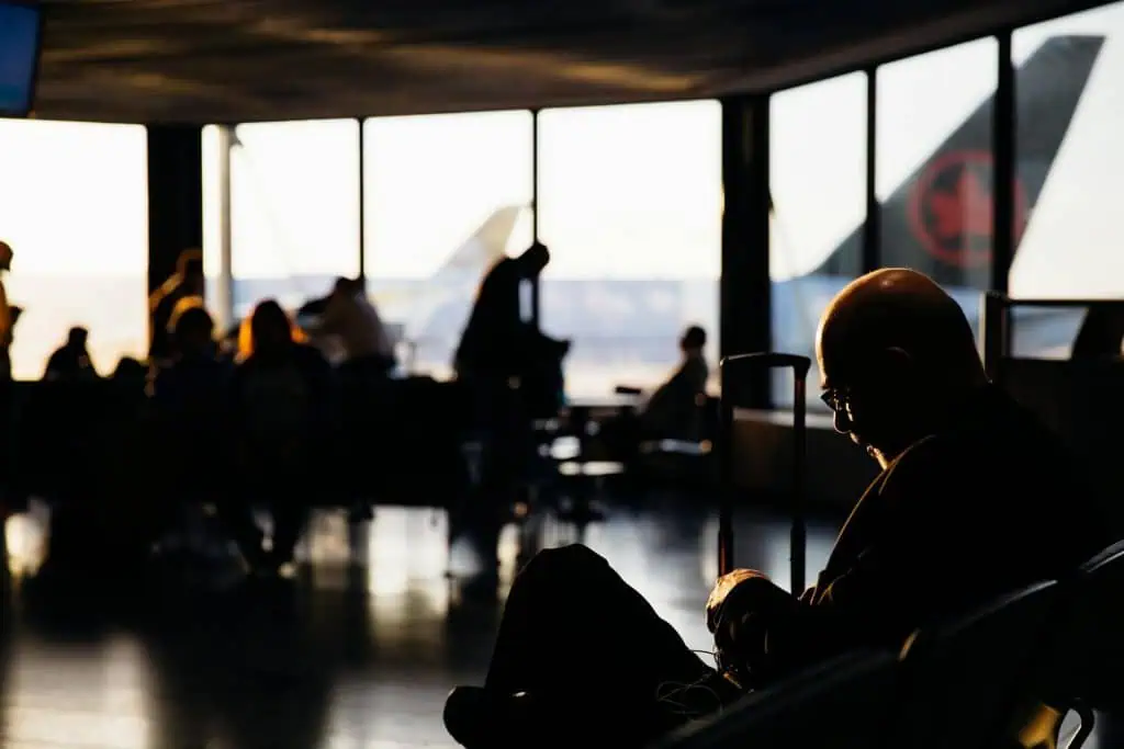 Travelers seated and waiting in an airport terminal, with warm sunlight casting shadows, reflecting the quiet tension and anticipation before a flight.