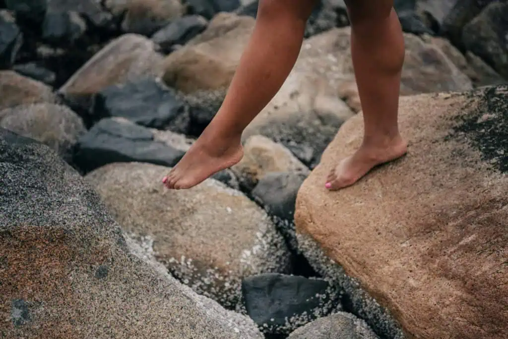 Close-up of a person balancing barefoot on large rocks, symbolizing vulnerability, uncertainty, or taking cautious steps.