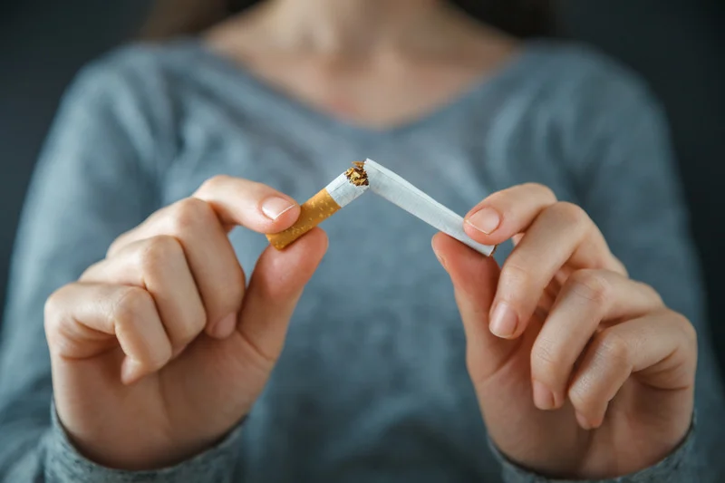 A woman in a grey sweater holds a broken cigarette between her hands, symbolizing the decision to quit smoking and embrace a healthier lifestyle.