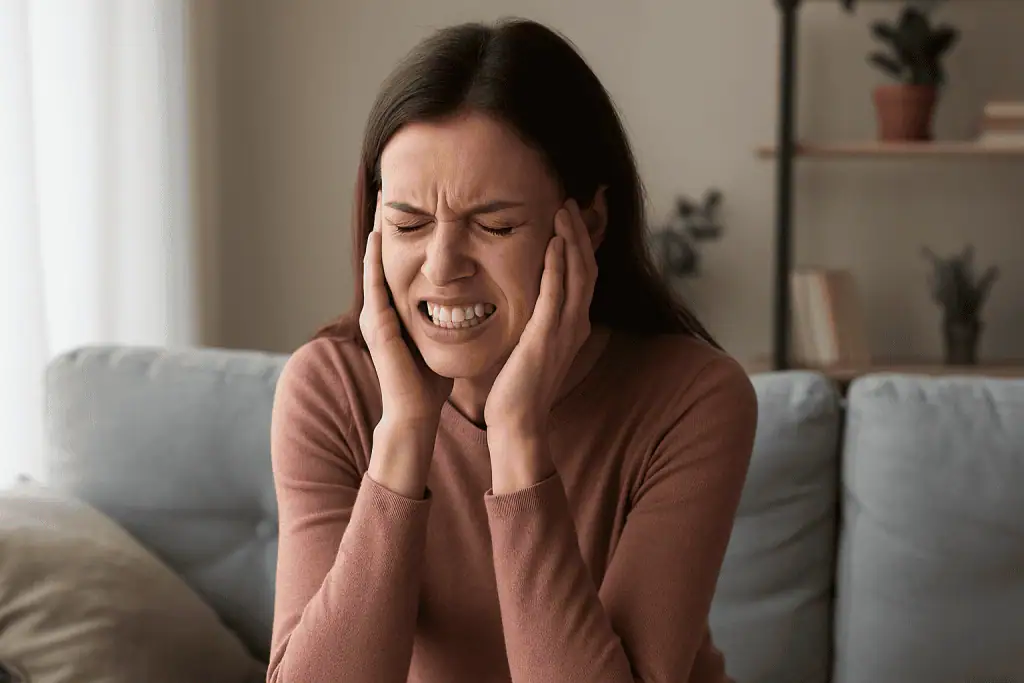 Woman holding her jaw in pain, showing signs of stress and teeth grinding (bruxism).