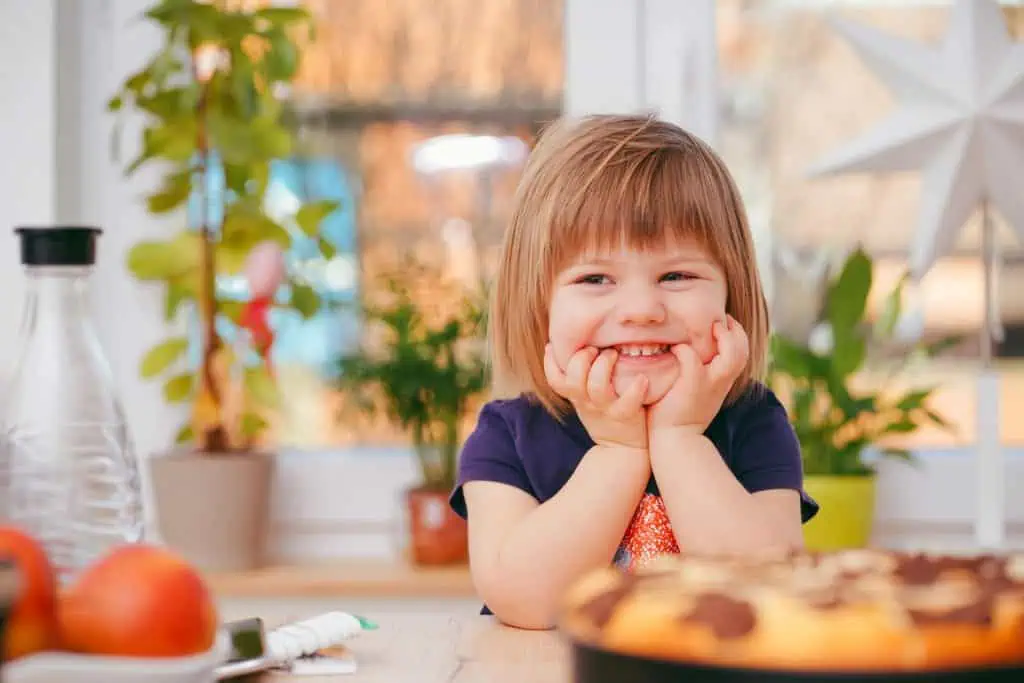 A young child smiling with their hands on their jaw, a common gesture seen in kids who may be experiencing jaw pressure related to bruxism.