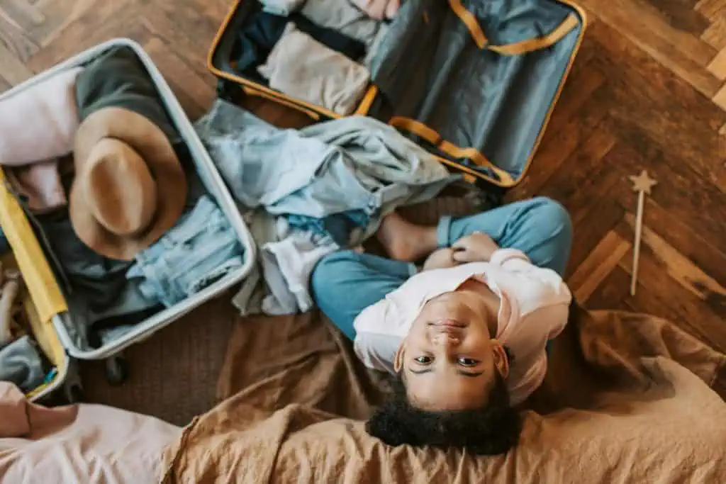 Young girl sitting calmly next to an open suitcase while packing for a trip, symbolizing relaxed flight preparation