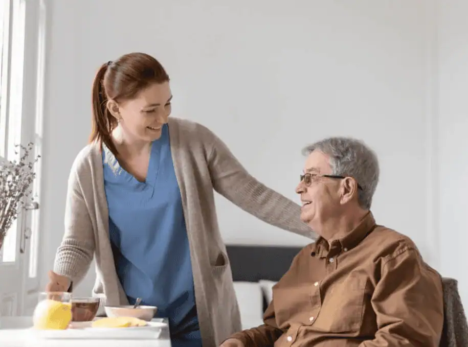 A caregiver assisting an elderly man with his meal while smiling in a cozy home setting.