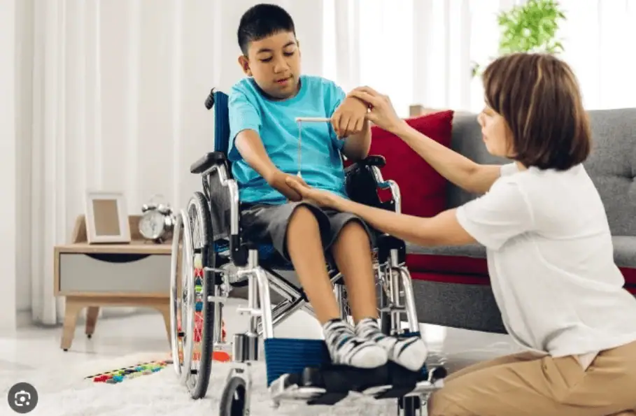 A young boy in a wheelchair receiving physical therapy from a caregiver in a home environment.