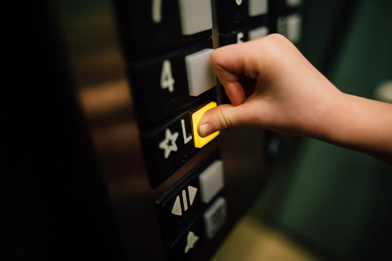 A child’s hand pressing the "L" button in an elevator panel.