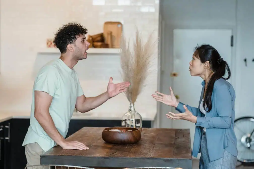 A man and woman arguing across a kitchen table, representing the emotional tension and communication challenges of co-parenting after separation.