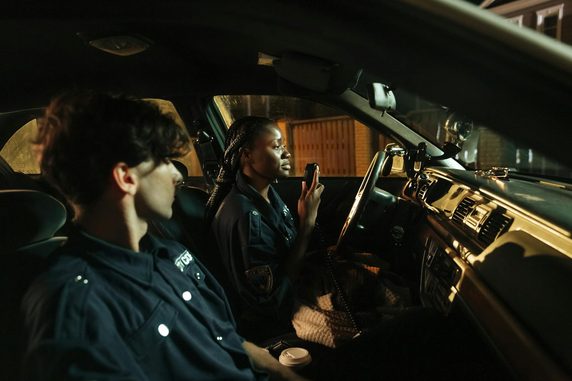 Two correctional officers inside a patrol car during a night shift, highlighting the demands and focus required in high-stress environments.