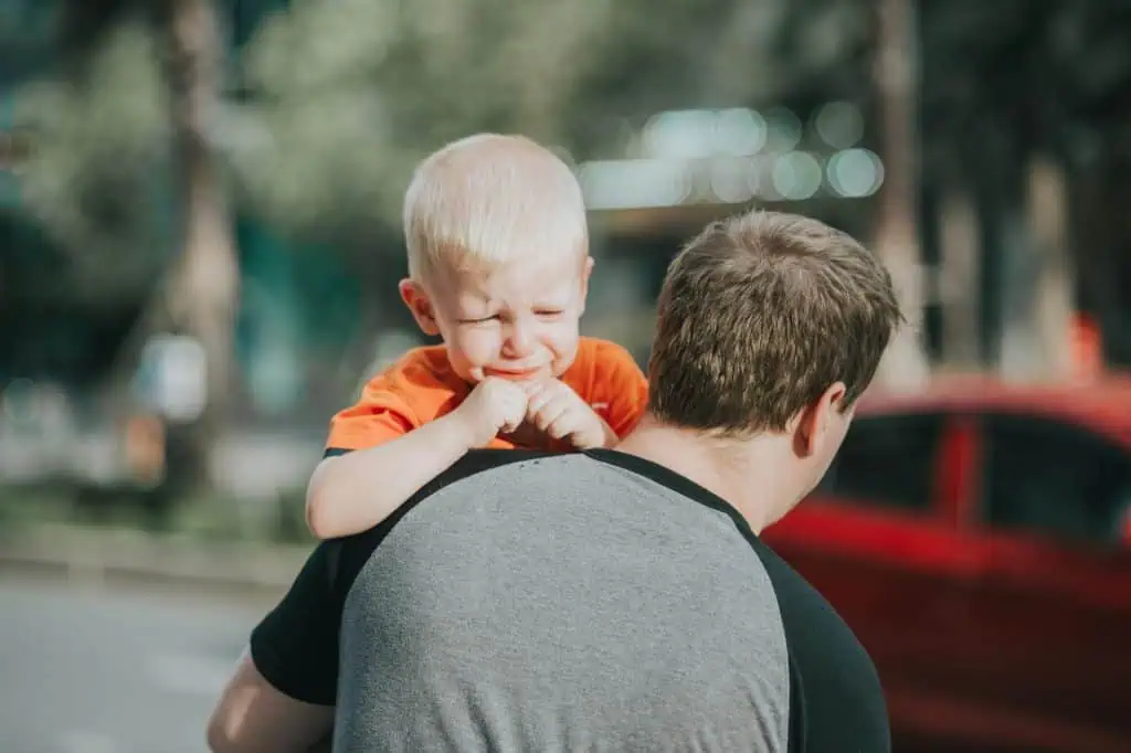 A young boy crying while being carried on his father’s shoulder, symbolizing the emotional impact of separation on children.