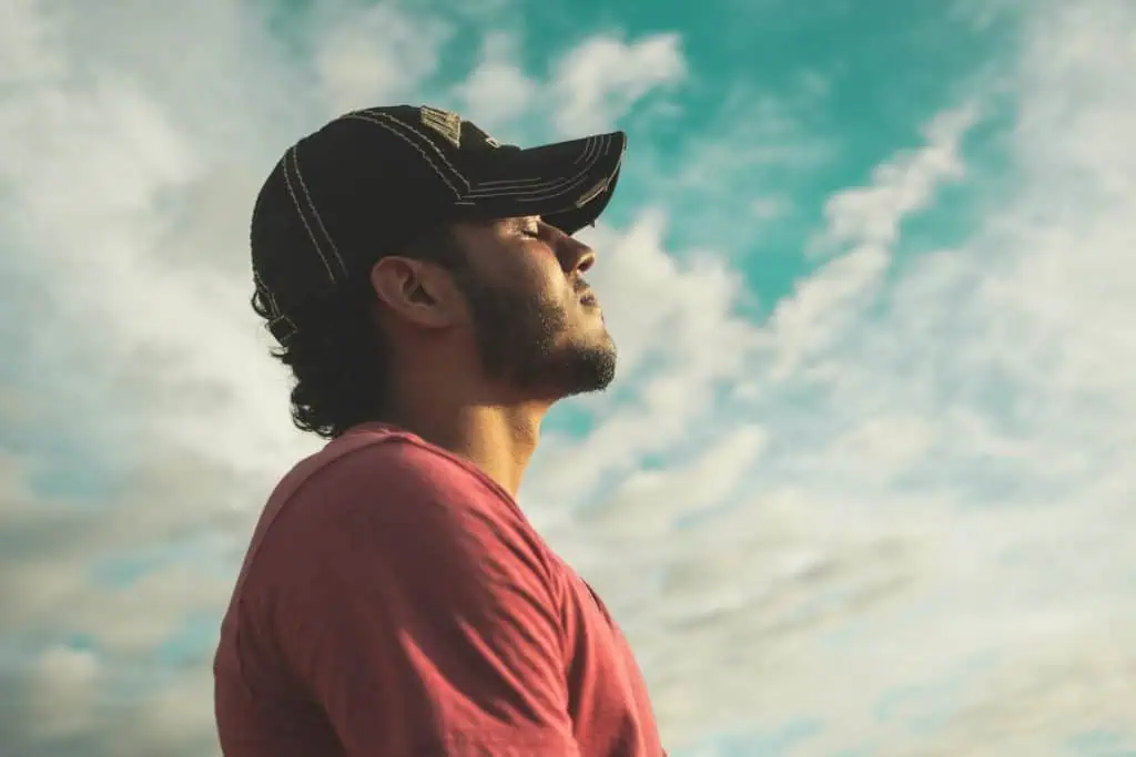 Man practicing deep breathing with eyes closed under the sky, symbolizing calmness and anxiety relief before flying