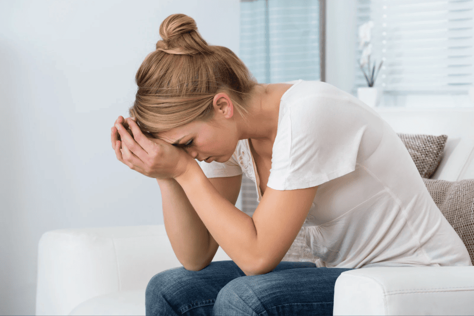 Woman sitting on a couch with head in hands, visibly overwhelmed or distressed.