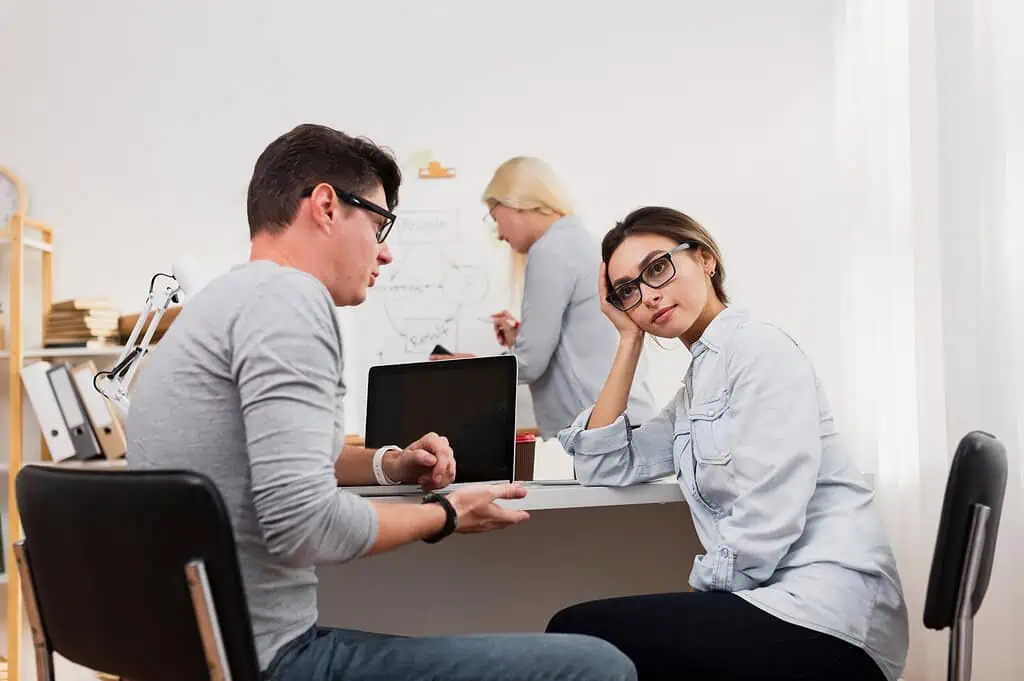 Woman looking frustrated during a workplace discussion while a colleague explains something, representing communication and organizational challenges faced by adults with dyspraxia.