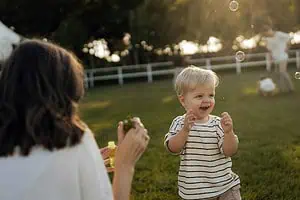 Smiling child playing with bubbles outdoors, supported by parent, symbolizing joy and growth, and dyspraxia in children.