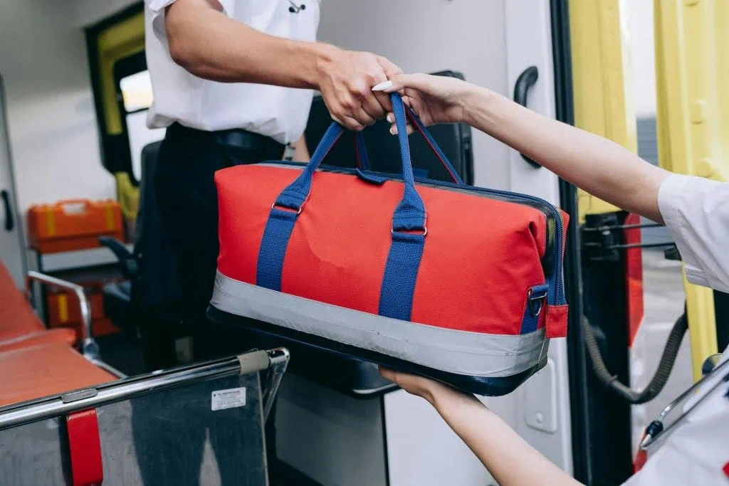 First Responder handing over a red and blue first aid bag inside an ambulance.