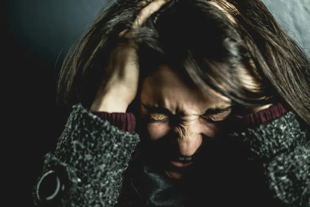 A person sits on the floor with their head buried in their knees and hands covering their head, illustrating an emotional breakdown or intense anxiety and stress response.