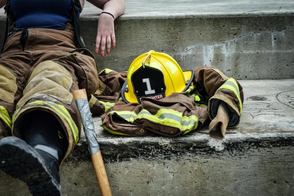 A first responder resting on concrete steps with turnout gear, helmet, and axe laid beside them, symbolizing emotional compartmentalization, exhaustion and the weight of the job. Compartmentalization