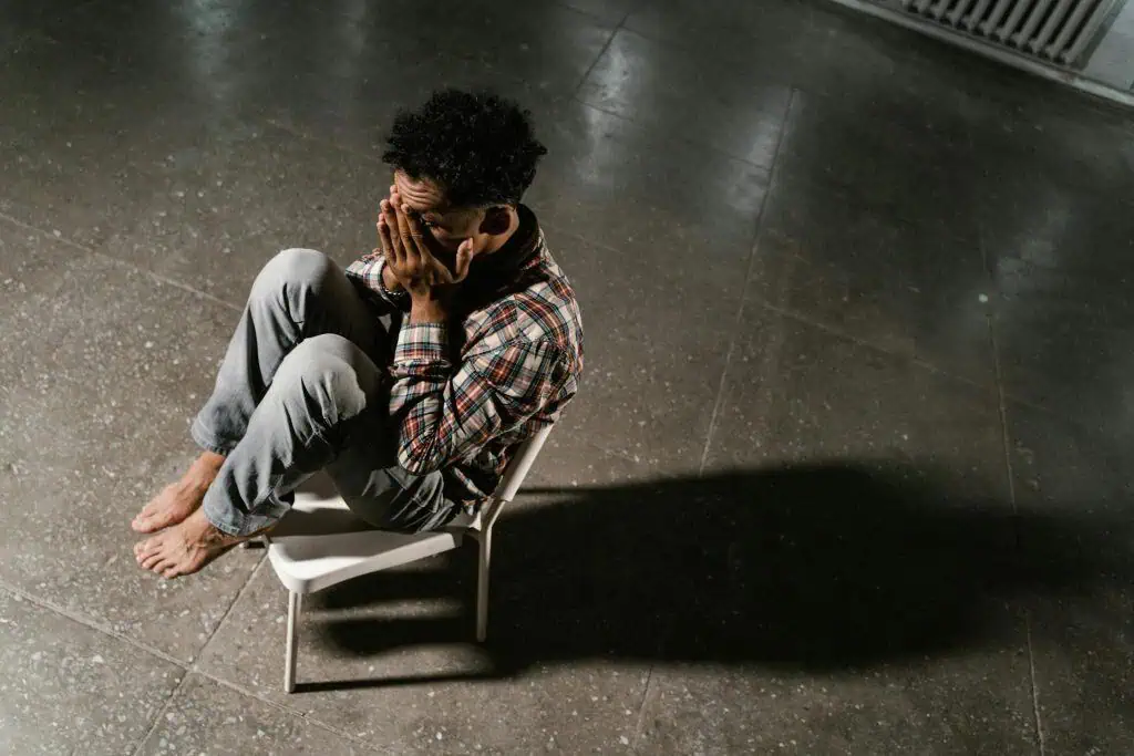 Man sitting barefoot on a chair with hands covering face, showing signs of emotional stress linked to bruxism