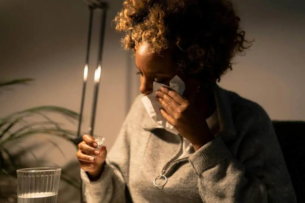 A stressed woman wiping her tears while holding a small vial, symbolizing the emotional toll that can contribute to TMJ pain.
