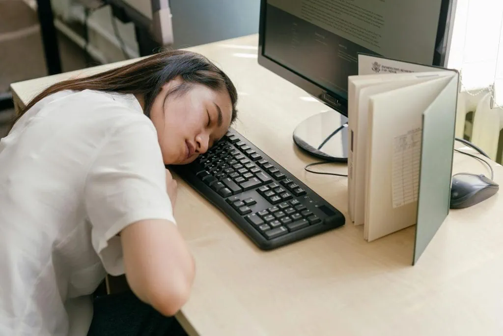 A person lies in bed with a relaxed expression while holding a smartphone, suggesting employer support for better sleep through wellness apps, flexible schedules, or mental health resource