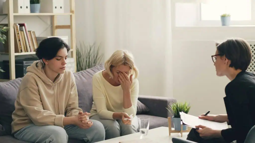 Teen and parent in an emotional family therapy session with a counselor in a calm office setting