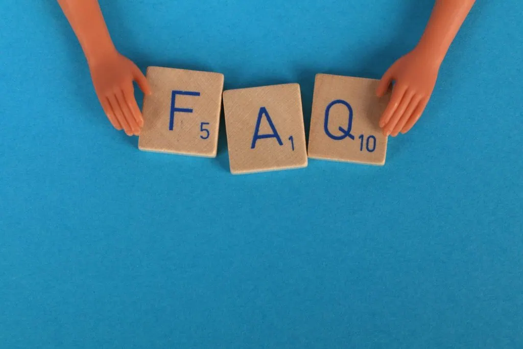 Wooden letter tiles spelling "FAQ" with toy hands on a blue background.