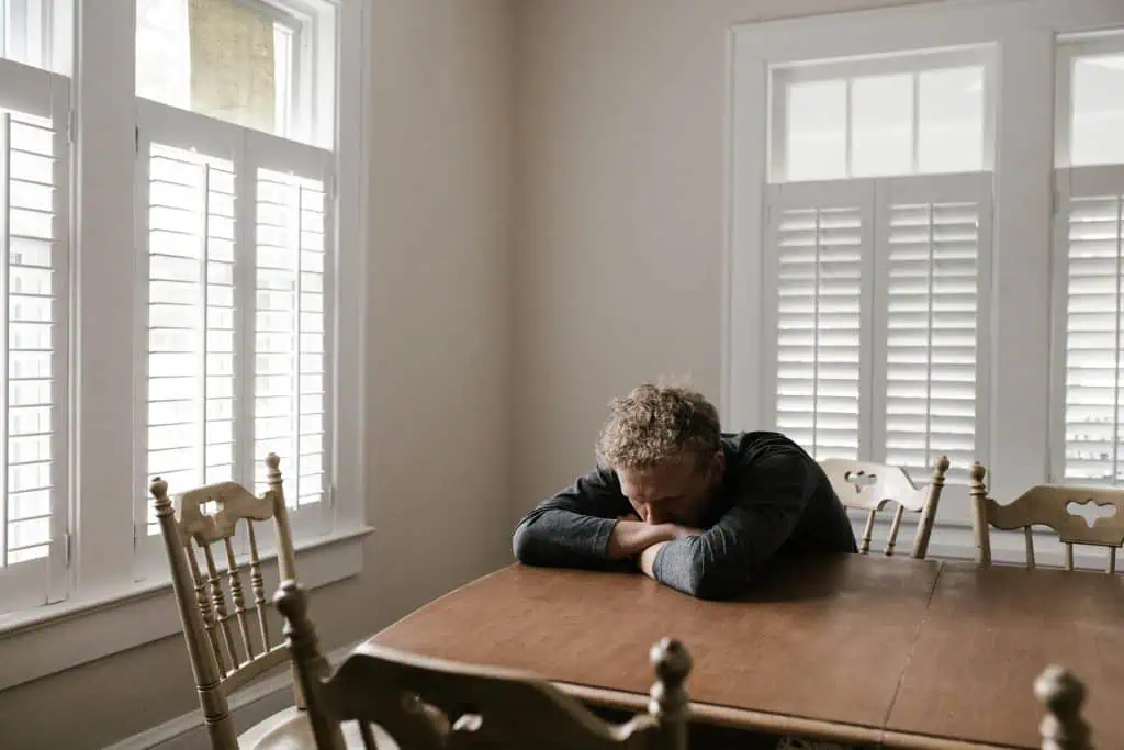 Man resting his head on a table in a bright room, appearing exhausted and anxious—possible causes of bruxism