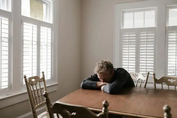 Man resting his head on a table in a bright room, appearing exhausted and anxious—possible causes of bruxism