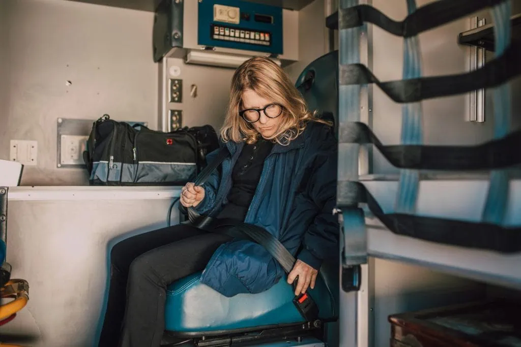 Female paramedic wearing glasses buckling her seatbelt inside an ambulance, preparing for duty.