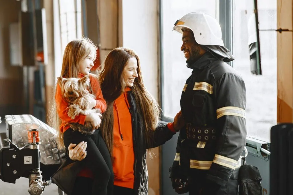 Smiling firefighter reconnecting with his wife and daughter at the station, highlighting strong family bonds after duty.