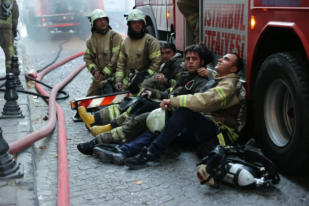 Firefighters resting near their truck after responding to an emergency, showing exhaustion from their heroic work