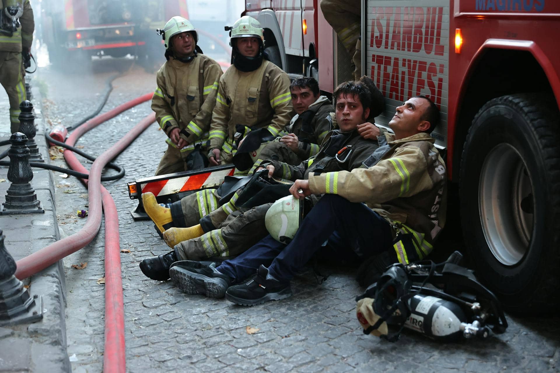 Firefighters resting near their truck after responding to an emergency, showing exhaustion from their heroic work