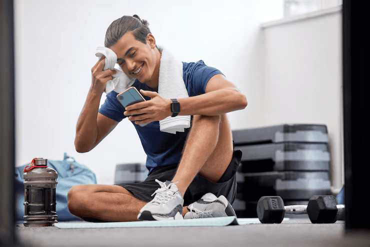 Fitness phone man with sweat social media gym training workout exercise resting break mobile app digital tired athlete relaxing cellphone searching body goals posts