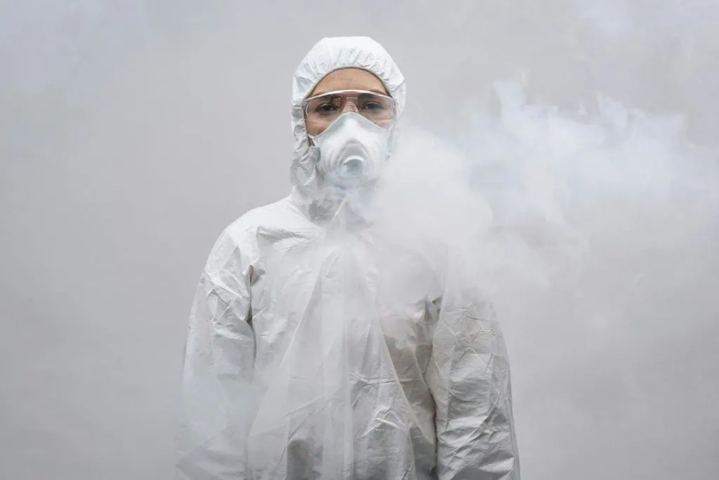Frontline worker wearing a hazmat suit and respirator mask, standing in a smoke-filled environment to represent high-risk emergency conditions.