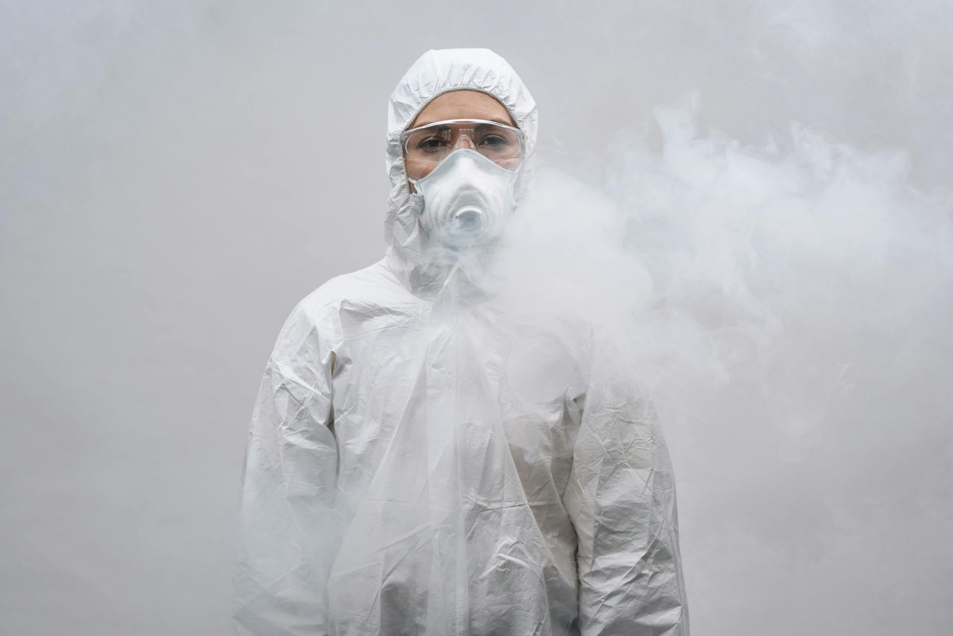 Frontline worker wearing a hazmat suit and respirator mask, standing in a smoke-filled environment to represent high-risk emergency conditions.
