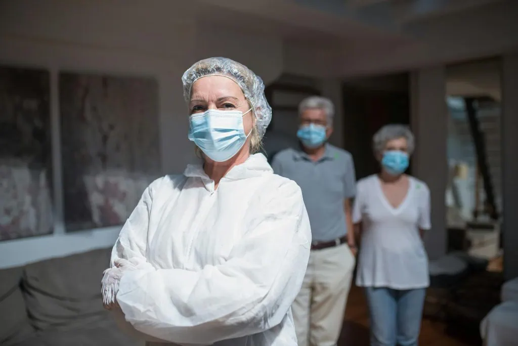 Frontline healthcare worker in protective gear and face mask standing confidently in front of her family at home during the pandemic. Hypnotherapy.